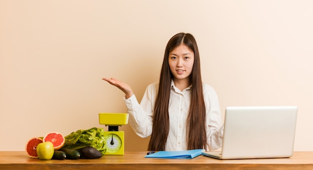 Donna cinese del giovane dietista che lavora con il suo computer portatile che dubita fra due opzioni.