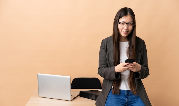 Donna cinese di affari nel suo posto di lavoro che invia un messaggio con il cellulare