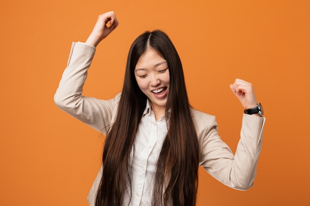 Donna cinese di giovani affari che celebra un giorno speciale, salti e alzando le braccia con energia.