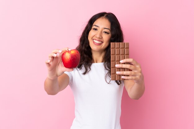Donna cinese spagnola che prende una compressa di cioccolato in una mano e una mela nell'altra