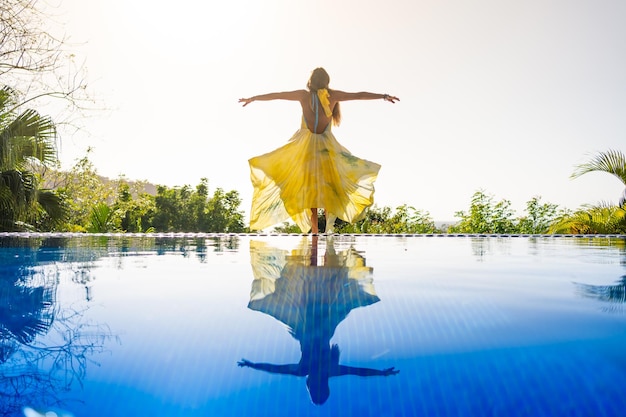 Donna con abito giallo che alza le braccia in una piscina all'aperto