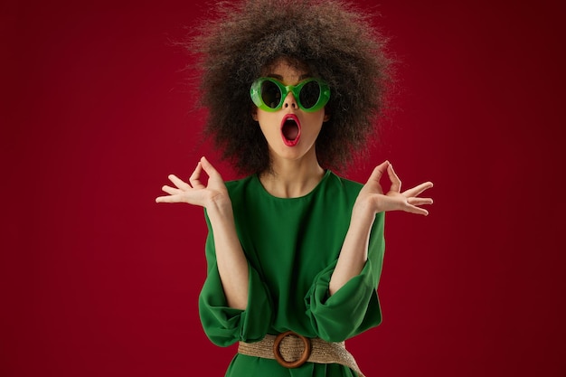 Donna con abito verde occhiali da sole acconciatura di moda sfondo rosso foto di alta qualità