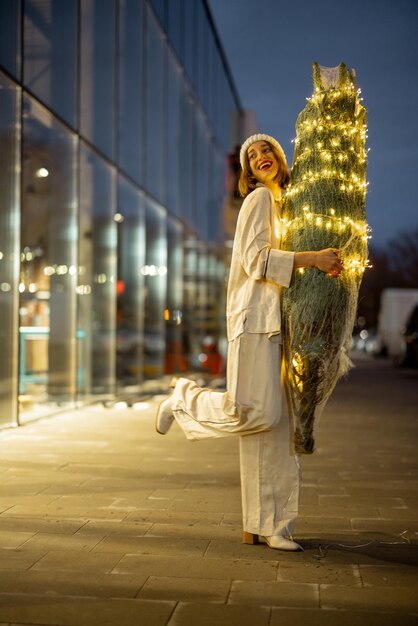 Donna con albero di Natale illuminato vicino al centro commerciale