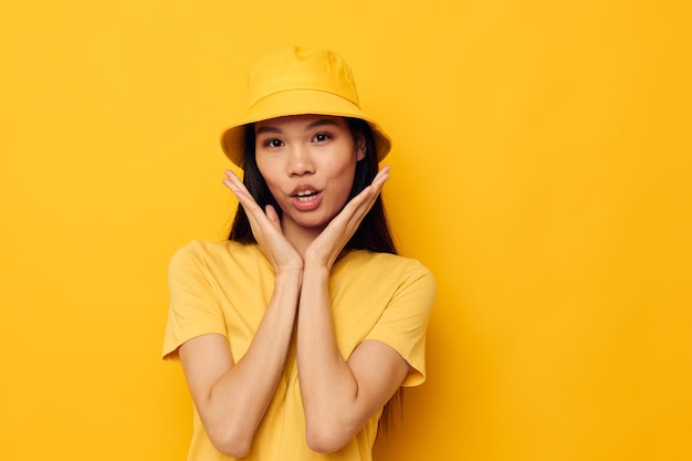 Donna con aspetto asiatico in una maglietta gialla e cappello in posa emozioni sfondo isolato inalterato