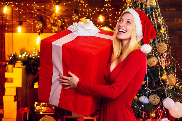 Donna con atmosfera natalizia. Giovane donna in vestito rosso elegante sopra l'interiore di Natale