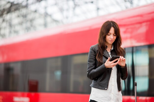 Donna con bagagli alla stazione che viaggiano in treno. Giovane turista con il cellulare e bagaglio sulla piattaforma in attesa di espresso