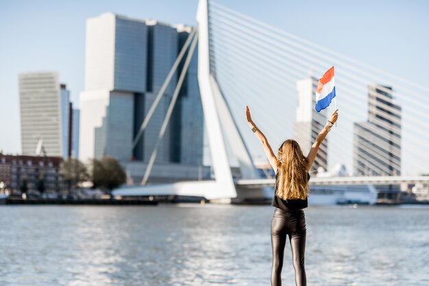 Donna con bandiera olandese che gode di una splendida vista del paesaggio urbano sulla moderna riva del fiume durante la mattinata nella città di Rotterdam