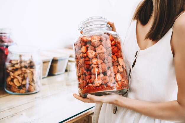 donna con barattoli di vetro che acquista bacche e frutti secchi in un negozio a rifiuti zero