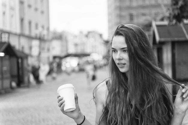 Donna con bevanda da asporto cammina per strada Donna sexy tiene una tazza di caffè usa e getta Ragazza di bellezza con capelli lunghi e trucco naturale Umore di caffè o tè Bevande e cibo durante le vacanze estive o in viaggio