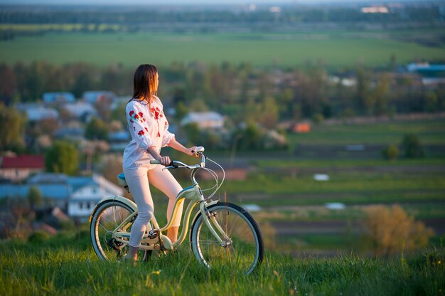 Donna con bici retrò sulla collina di sera