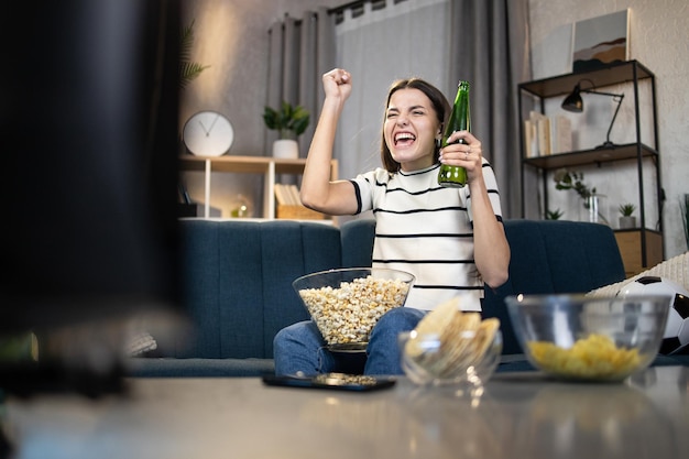 Donna con birra e spuntini che guardano la partita di calcio in TV