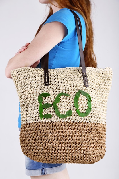 Donna con borsa ecologica in vimini estiva su sfondo grigio muro