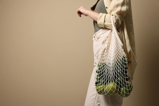 Donna con borsa ecologica piena di prodotti su sfondo beige primo piano Spazio per il testo