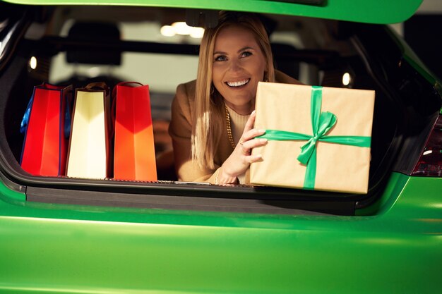 donna con borse della spesa e regali di Natale che giace nel bagagliaio sul parcheggio