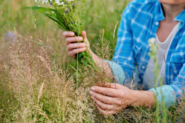 Donna con bouquet di erbe di campo e fiori che toccano piante in fiore nel campo estivo