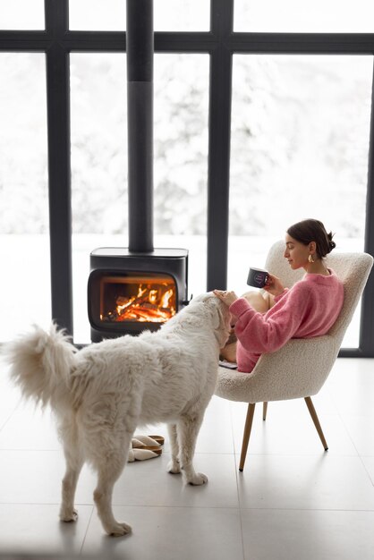 Donna con cane a casa con caminetto acceso durante l'inverno