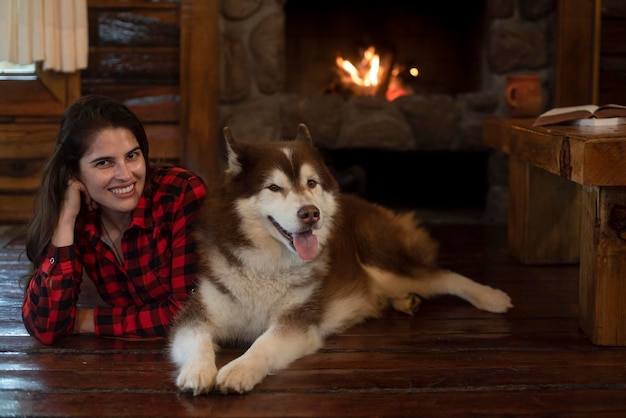 Donna con cane husky siberiano seduto sul pavimento di legno davanti al caminetto acceso