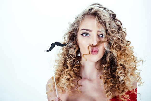 Donna con capelli ricci. Ritratto della ragazza divertente dei capelli ricci con i baffi sul bastone. Trucco e cosmetici per la cura della pelle. Bellezza e stile. Cura professionale dei capelli. Parrucchiere. Pubblicità da barbiere.