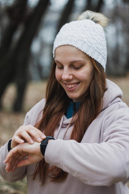 Donna con cappello bianco che controlla lo smartwatch durante una corsa invernale nel parco