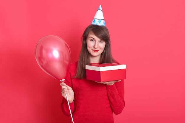 donna con cappello compleanno sulla testa, con palloncino rosso e confezione regalo