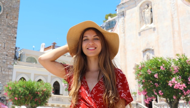 Donna con cappello di paglia e abito rosso con il villaggio di Taormina, Sicilia, Italia
