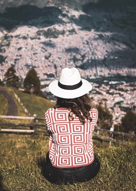 donna con cappello e maglione seduta guardando il paesaggio sulla collina