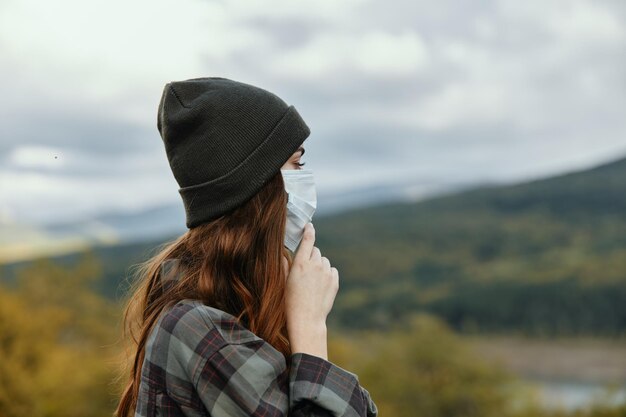 Donna con cappello e maschera medica camicia a scacchi montagne natura autunno