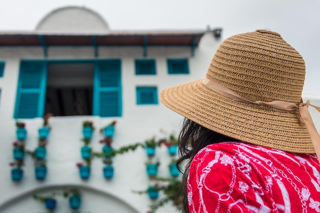 Donna con cappello e vestito rosso che guarda una finestra da dietro