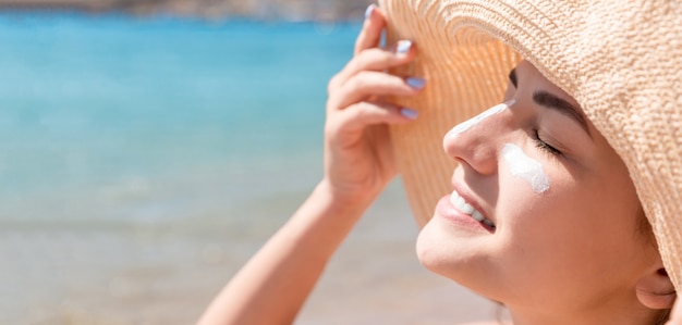donna con cappello sta applicando crema solare sotto gli occhi