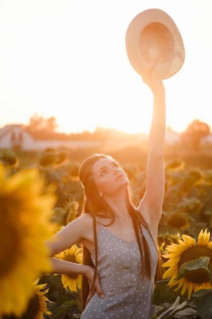 Donna con cappello sul campo di girasole giovane persona allegra che tiene le mani in aria e guarda