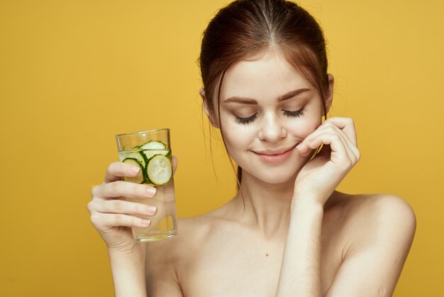 Donna con cetriolo bere vitamine cura del corpo sfondo giallo