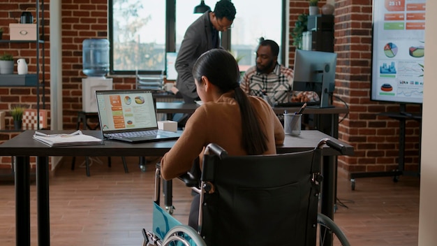 Donna con disabilità fisica che esamina grafici e grafici sullo schermo del laptop, lavorando con le statistiche per pianificare l'analisi e la strategia di marketing. Giovane che utilizza le informazioni del diagramma.