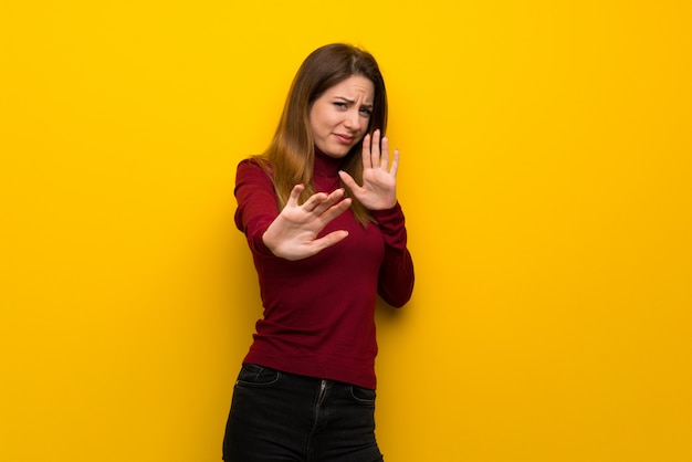 Donna con dolcevita sul muro giallo nervoso e spaventato allungando le mani verso la parte anteriore