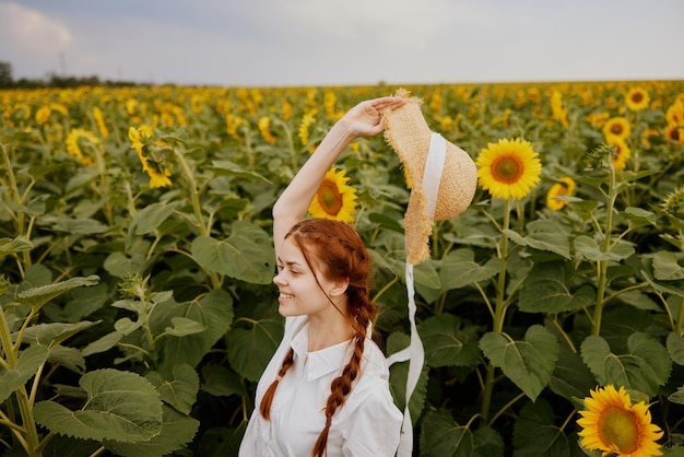 Donna con due trecce in un cappello di paglia in un abito bianco un campo di girasoli agricoltura Ora legale