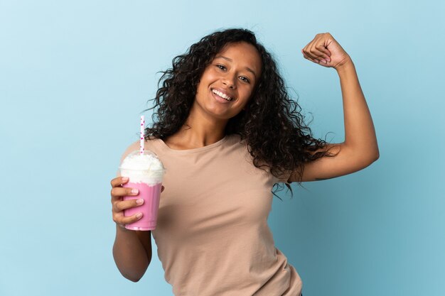 Donna con frappè alla fragola isolato sull'azzurro che fa forte gesto