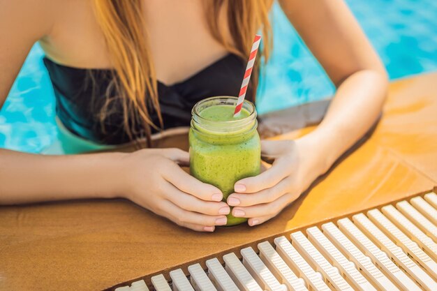 Donna con frullati verdi di spinaci e banana sullo sfondo della piscina Frullati sani di cibo sano