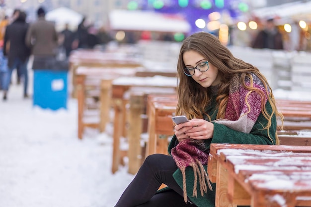 donna con gli occhiali con un telefono in mano a un tavolo in una città d'inverno