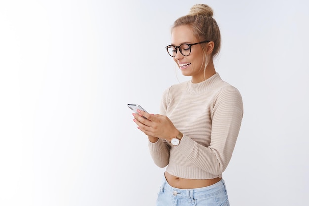 Donna con gli occhiali ridere come smartphone di messaggistica sorridente ampiamente essendo di buon umore divertendosi a chattare online tramite telefono cellulare su white