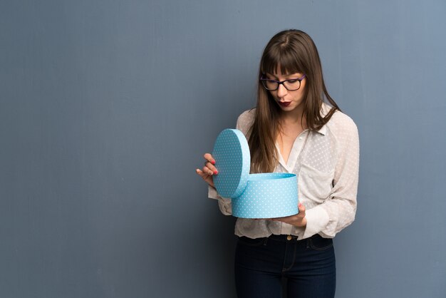 Donna con gli occhiali sopra la parete blu che tiene un regalo in mano