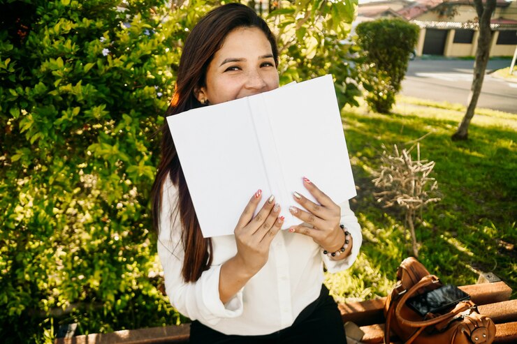 Donna con graziose lentiggini sorridente e nascondendo il viso con un libro