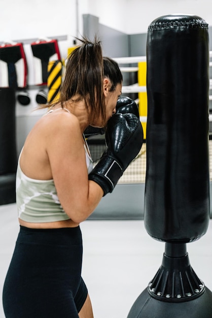 Donna con guantoni da boxe neri che si esercitano con un sacco da boxe in palestra