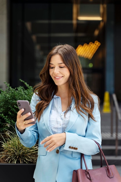 donna con i capelli in giacca blu con un messaggio di testo sul cellulare che controlla la posta in strada