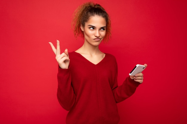 donna con i capelli ricci raccolti che indossa un maglione rosso scuro isolato su rosso