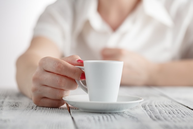 Donna con i chiodi rossi che si siedono e che tengono una tazza di caffè calda