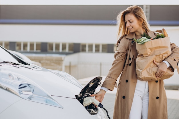 Donna con i sacchetti della spesa alimentare che carica l'auto elettrica