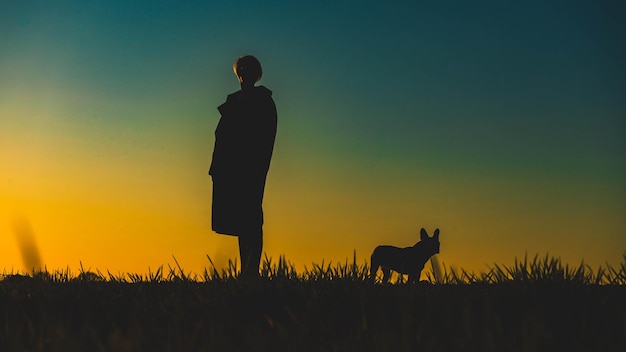 Donna con il cane in piedi sul campo contro il cielo durante il tramonto