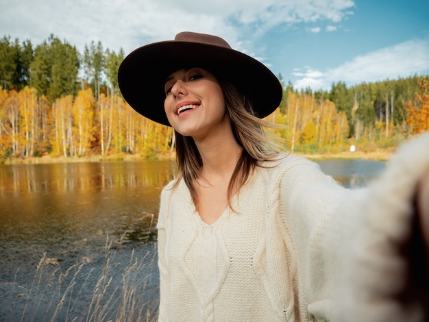 Donna con il cappello vicino al lago nel tempo di autunno