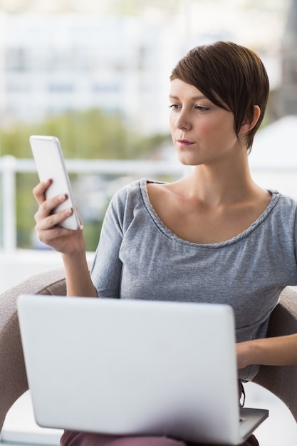 Donna con il computer portatile che per mezzo del telefono cellulare