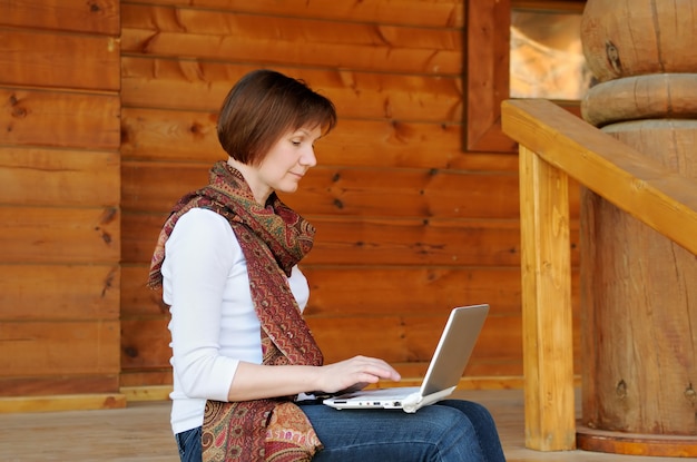 Donna con il portatile seduto sul portico in legno