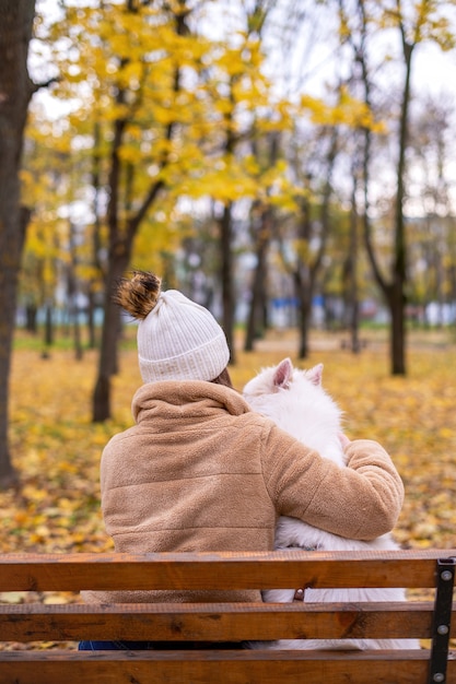 Donna con il suo cane in autunno in un parco. La donna lo sta abbracciando in panchina.